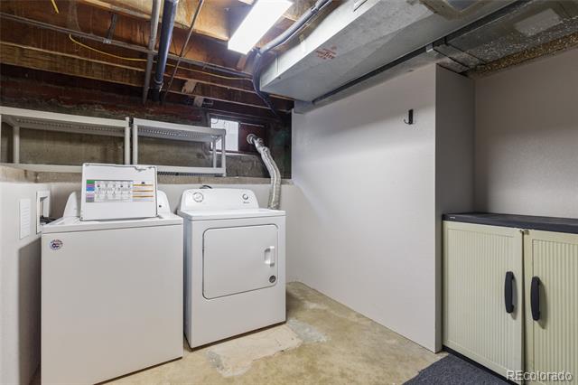 Basement laundry area with washer and dryer beside cream storage cabinets.