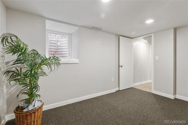 Empty carpeted room with a small window, open doorway, and potted palm.