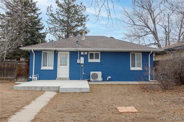 Rear exterior of a blue single-story house with a concrete patio and path through a dormant yard.