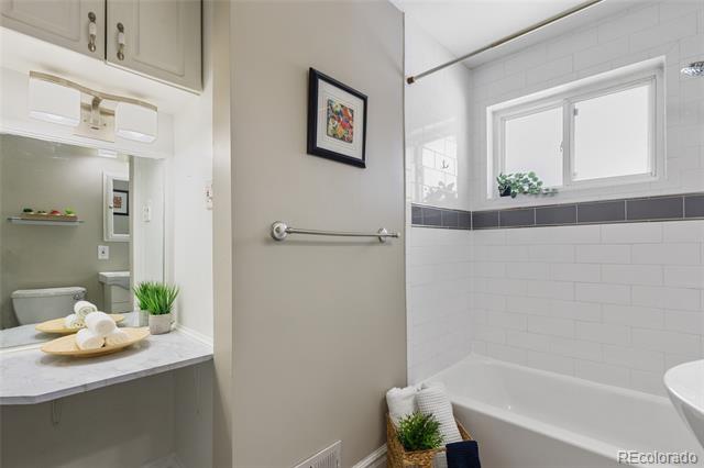 Bathroom with white tiled tub, dark accent stripe, and separate vanity with plants and towels.
