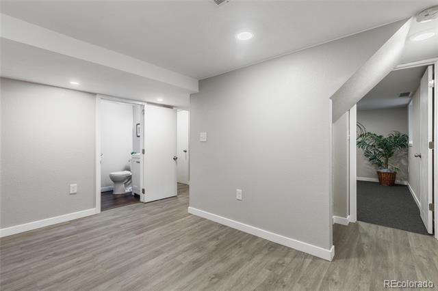 Interior room with gray wood-look flooring, an open bathroom door, and a hallway with a potted plant.