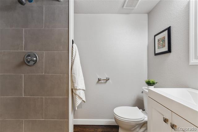Bathroom with a tiled shower, white toilet, and vanity topped with a small plant.