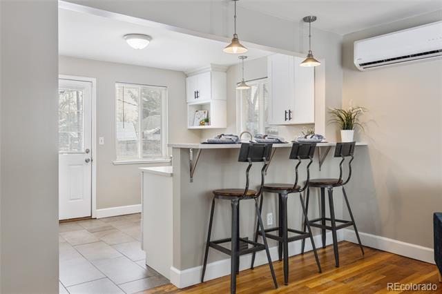Kitchen with a white peninsula, three bar stools, pendant lights, and hardwood flooring.