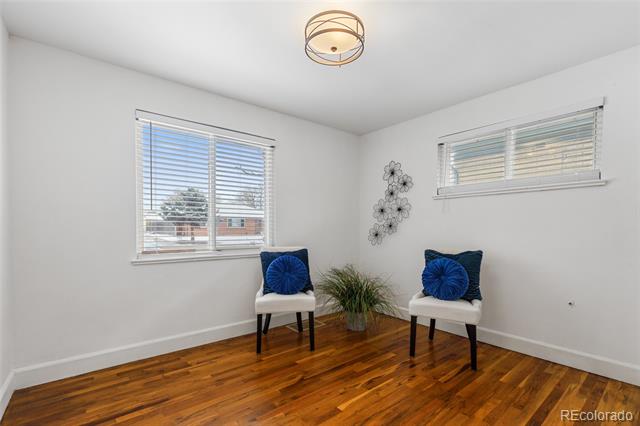 Furnished room with hardwood floors, two white chairs with blue cushions, and windows with blinds.