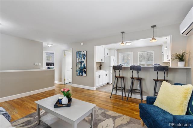 Living room with hardwood floors, a blue armchair, and an open kitchen with breakfast bar.