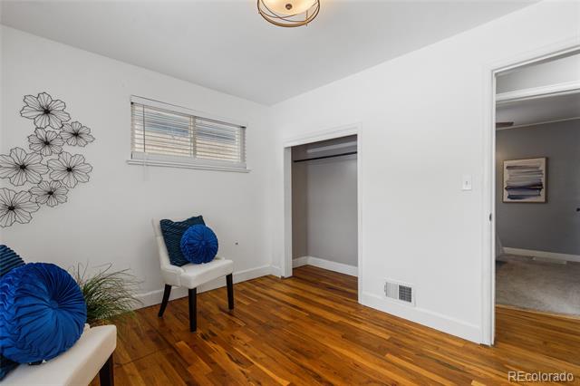 Small room with polished hardwood floors, blue-cushioned chairs, floral wall art, and an open closet.