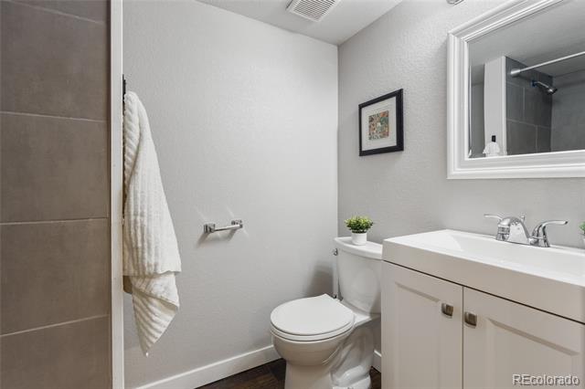 Bathroom with a white vanity and framed mirror beside a toilet and tiled shower.