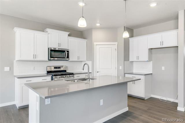 Vacant kitchen with a large gray island, white cabinetry, and stainless steel appliances.