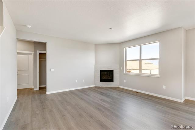 Empty living room with gray flooring, a corner fireplace, and a large window.