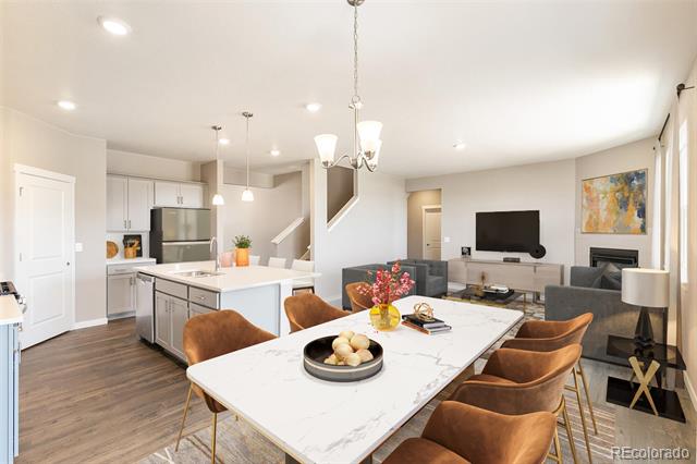 Open-plan dining area with a marble-look table, brown chairs, and kitchen and living room beyond.