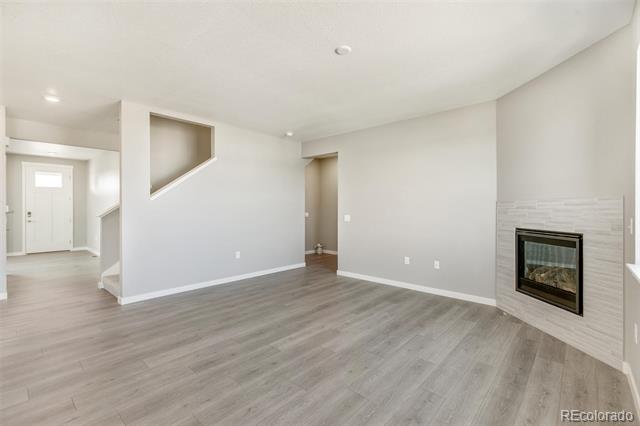 Vacant living room with gray flooring, a tiled fireplace, and an entryway beside the staircase.