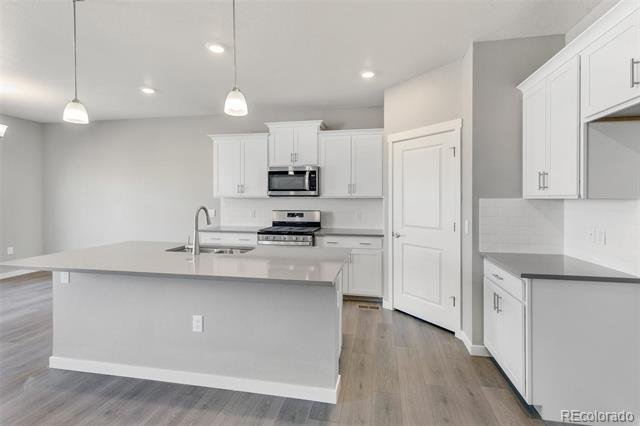 Empty kitchen with white cabinets, stainless steel appliances, and a large island.