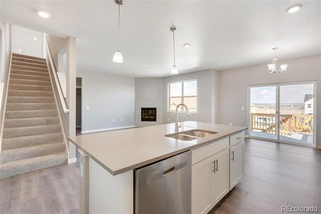 Open-plan kitchen with a large white island, carpeted staircase, fireplace, and sliding doors to a deck.