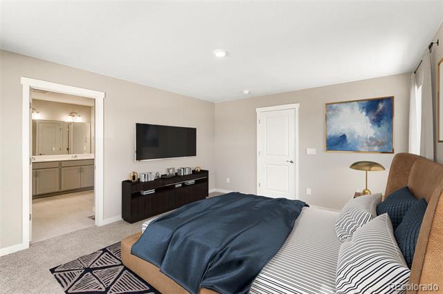 Bedroom with a dark blue comforter, wall-mounted TV, and open doorway to a bathroom vanity.