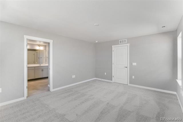 Empty carpeted room with gray walls, a white door, and an open doorway to a bathroom vanity.