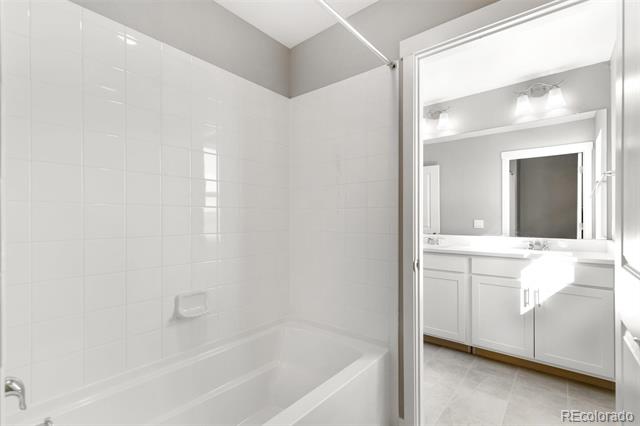 Bathroom with a white tiled tub-shower and adjoining vanity with a large mirror.