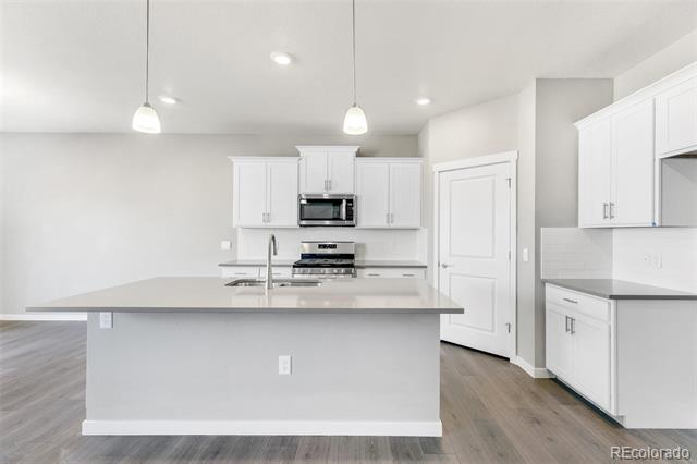 Kitchen with a large island, white cabinets, stainless steel appliances, and wood flooring.