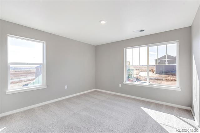 Empty bedroom with gray walls, pale carpet, and two windows overlooking a neighboring house.