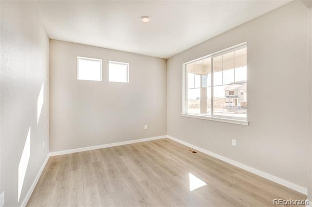 Empty room with light wood flooring, two high windows, and a large side window.
