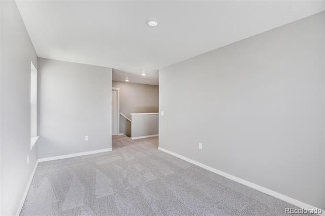 Empty carpeted room with gray walls and an open passage to an adjoining area.
