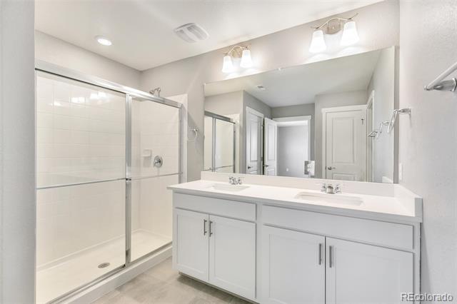 Bathroom with a white double-sink vanity and glass-enclosed tiled shower.