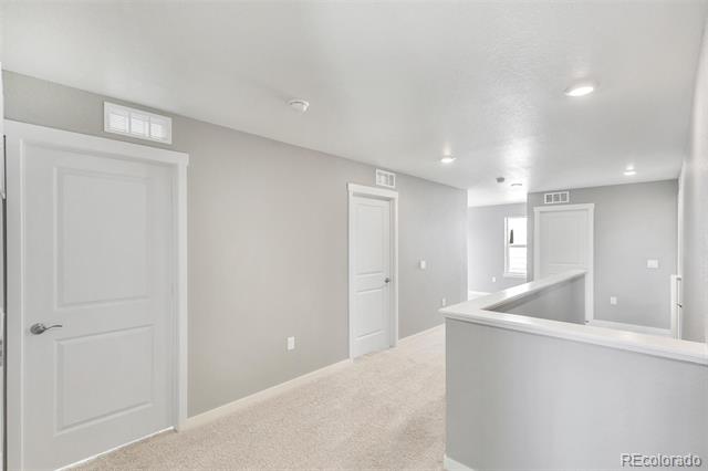 Vacant upstairs hallway with beige carpet, white paneled doors, and a half-height railing.