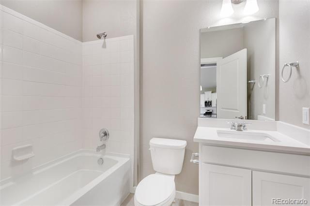 Bathroom with a white bathtub, toilet, and vanity beneath a large mirror.