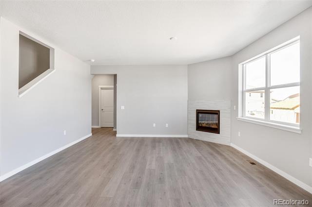 Vacant living room with a built-in fireplace, gray wood-look floors, and a large window.