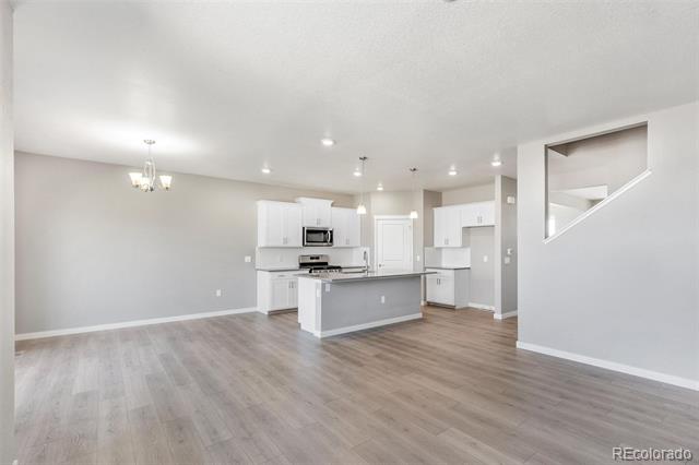 Open-plan kitchen with a central island, white cabinets, and wood-look flooring.