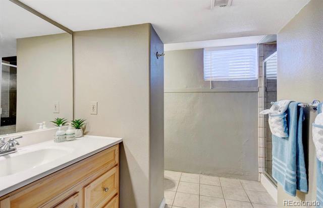 Bathroom with a light wood vanity, tiled shower, and blue towels.