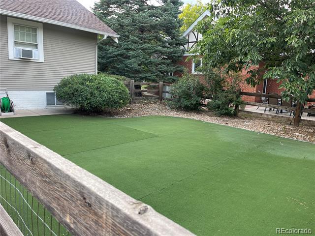 Backyard putting green with artificial turf, a low wooden fence, and mature trees.