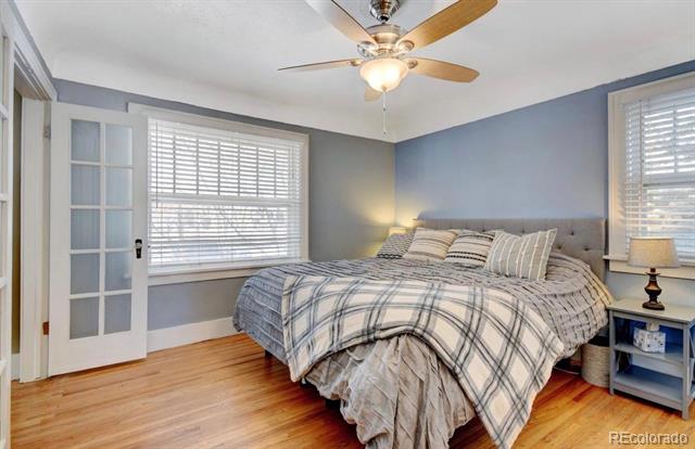 Bedroom with plaid bedding, light wood floors, two windows, and a ceiling fan.