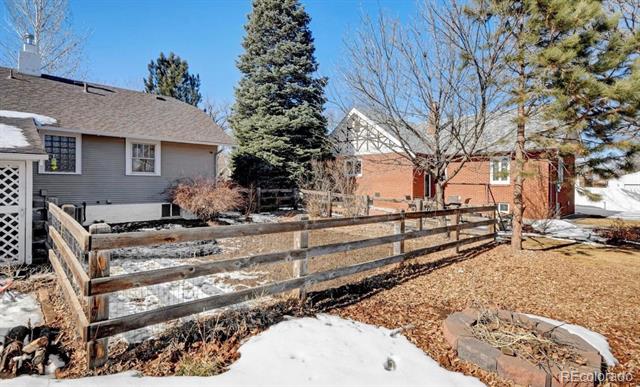 Fenced yard with patches of snow and fallen leaves, framed by bare trees and neighboring homes.