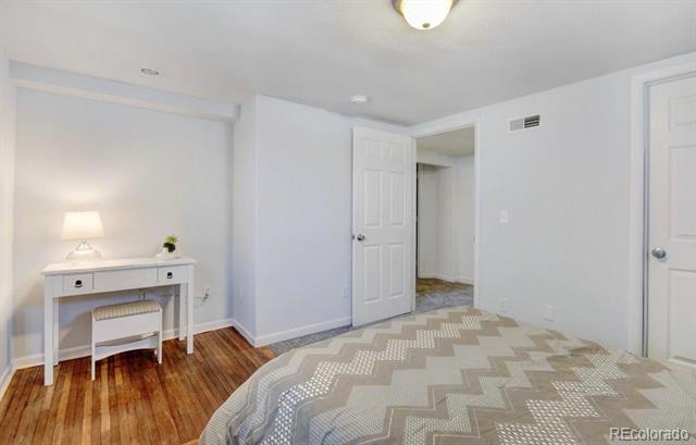 Bedroom with a geometric quilt, hardwood floor, and a small desk beside the bed.