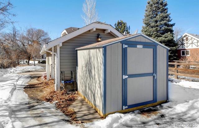 Gray storage shed with blue trim beside a snow-covered path.