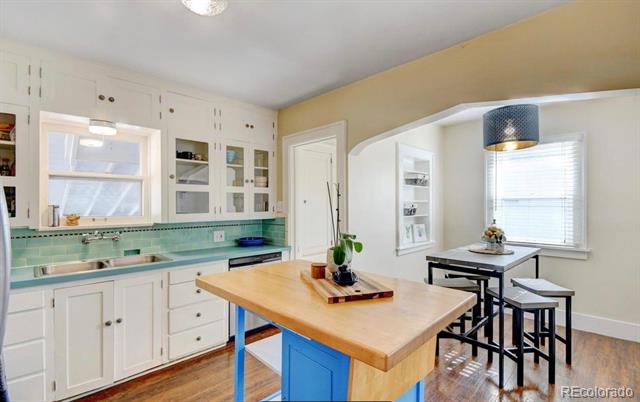 Kitchen with a wood-topped blue island, white cabinetry, mint-green backsplash, and dining stools by the window.