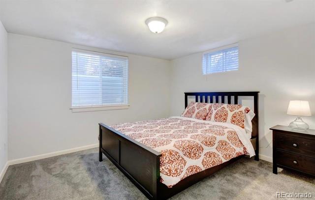 Bedroom with a dark wood bed, rust-and-cream patterned bedding, gray carpet, and shuttered windows.