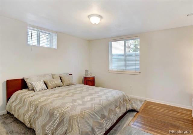 Bedroom with a large patterned bed, two windows with blinds, and hardwood flooring.