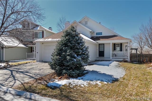 Two-story home with attached garage, covered porch, and evergreen amid patches of snow.