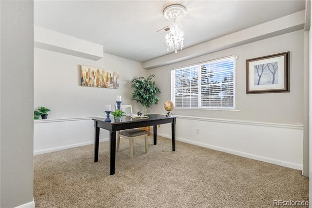 Staged home office with a black desk, beige carpeting, and a chandelier.