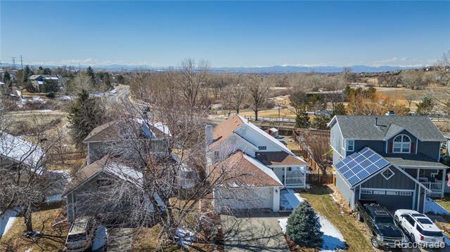Aerial view of detached homes with solar panels, patches of snow, and distant mountains.