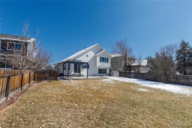White two-story home's rear exterior beyond a fenced, snow-dusted backyard.