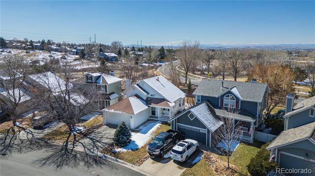 Aerial view of a blue-gray two-story home with an attached garage and patchy snow.
