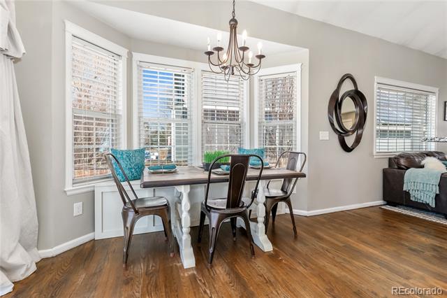 Dining area with a white table, metal chairs, hardwood floors, and a chandelier beneath tall windows.