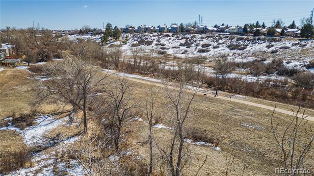 Snow-dusted meadow with leafless trees and a paved path, homes visible on the distant hillside.