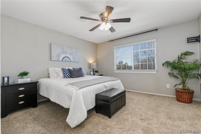 Staged bedroom with a king bed, black furniture, ceiling fan, and window with white blinds.