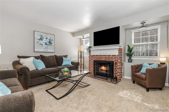 Living room with a brick fireplace, mounted TV, brown seating, and daylight through two windows.