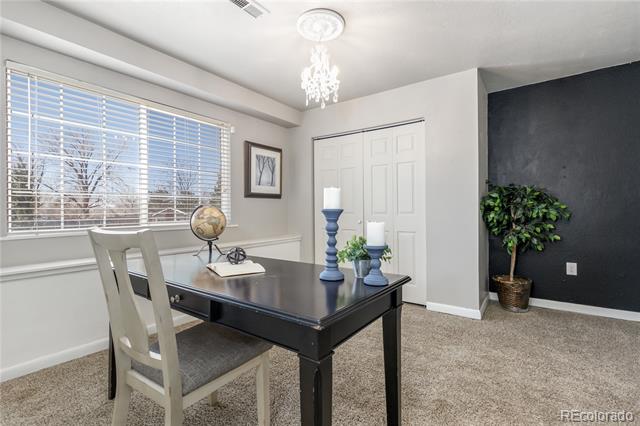 Home office with a black desk, large blinded windows, and a potted tree against a dark accent wall.