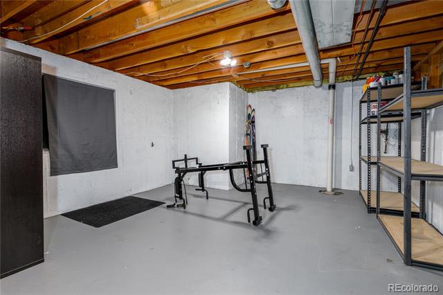 Unfinished basement gym with a weight bench, floor mat, and metal storage shelving.