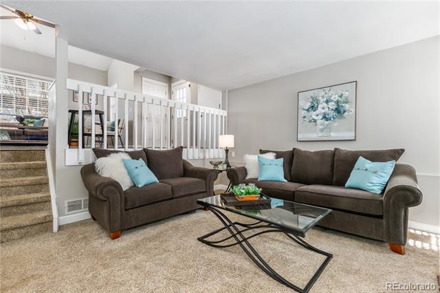 Living room with brown sofas, turquoise pillows, and a glass coffee table beside a white railing.
